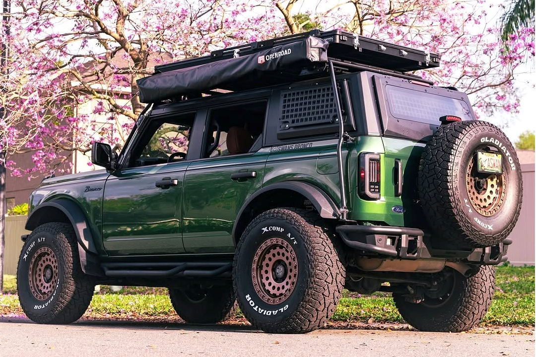 Ford Bronco with mounted Openroad 180-degree car awning in closed position, parked under blooming trees on a spring day