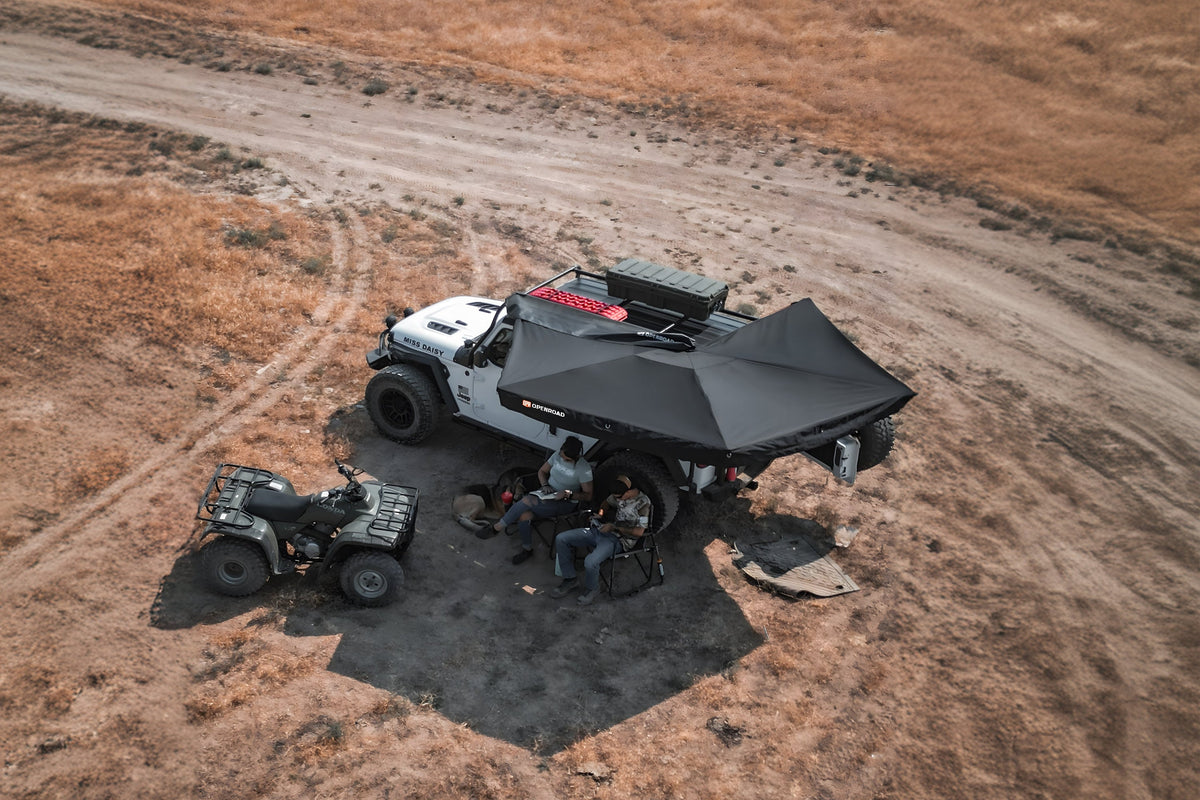 Outdoor scene of a 4WD Jeep fitted with Openroad 270-degree awning, providing shade for campers on an off-road trail with ATV nearby