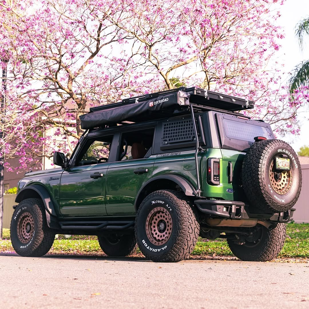 OPENROAD 180-degree free-standing car awning installed on a vehicle, offering full coverage shade and weather protection in a beautiful outdoor landscape with blooming trees.