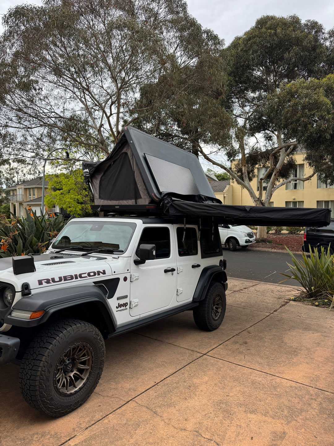 Jeep Wrangler JL Rubicon fitted with an Openroad 270 awning and rooftop tent, parked on a driveway.