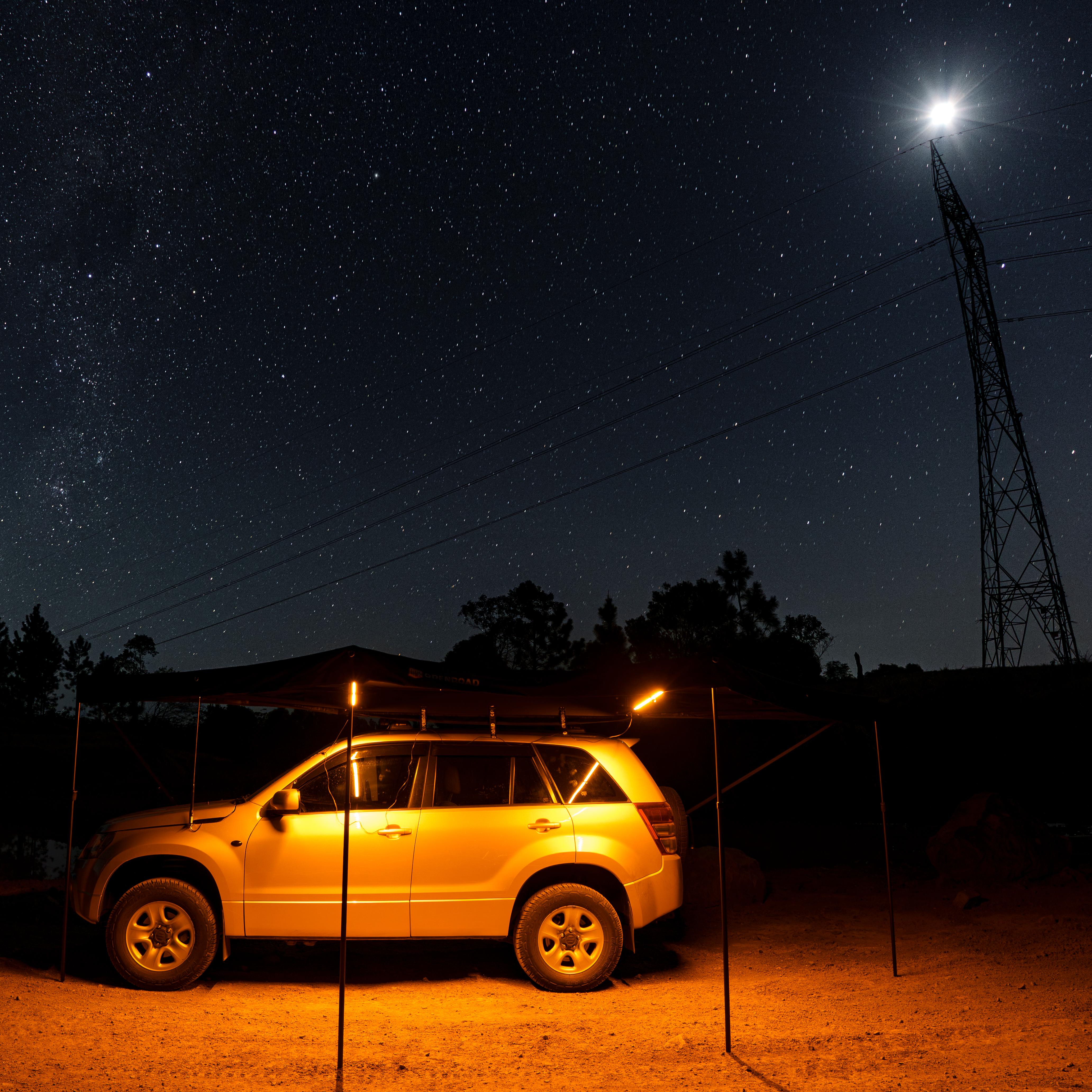 OPENROAD 180 awning at night on a 4WD, warm amber camp light under a starry sky 