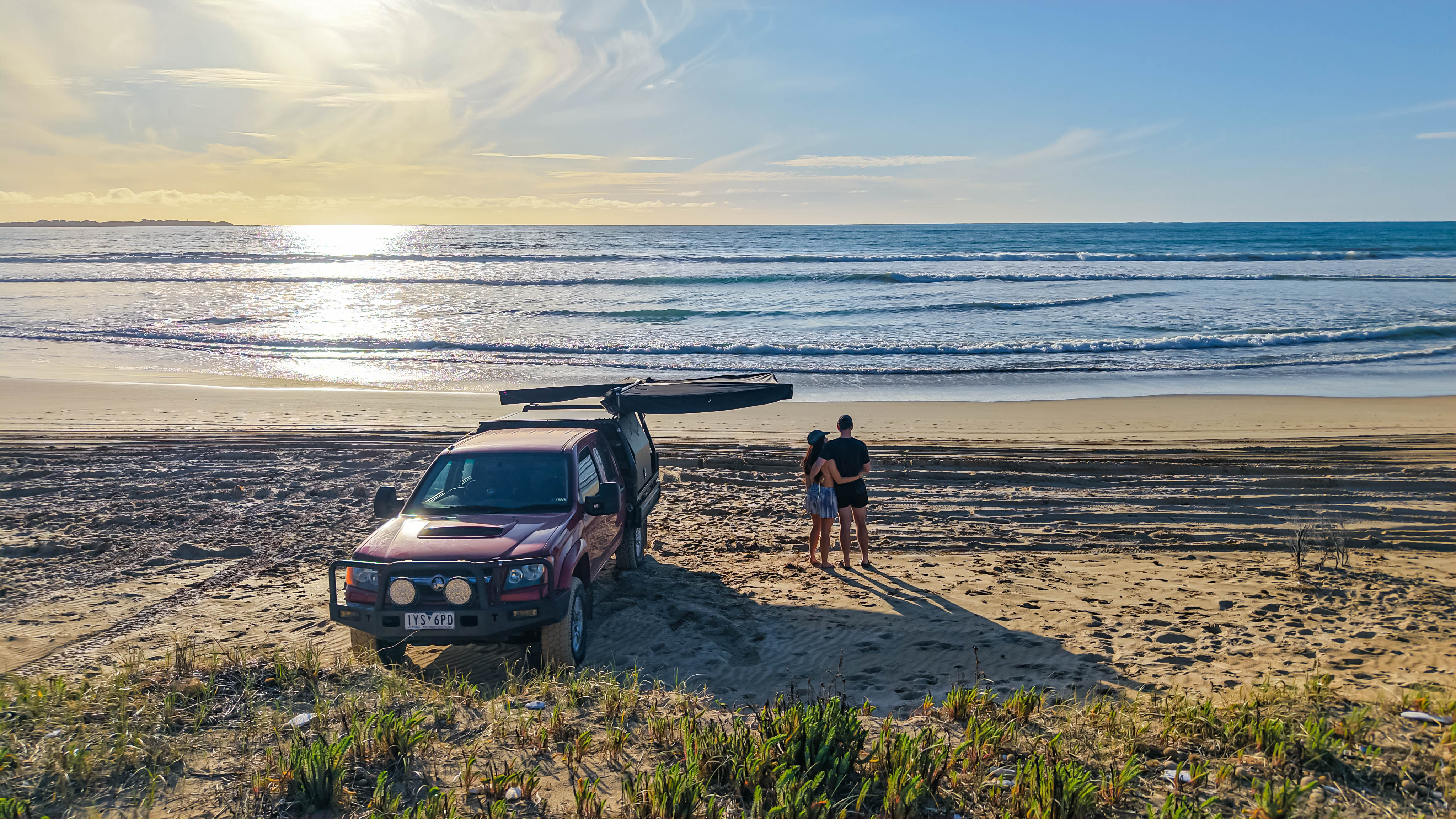 OPENROAD 270 awning on a modified Holden Colorado RC dual cab at the beach; roof-rack mounted as a couple watch the surf, ready for coastal camping