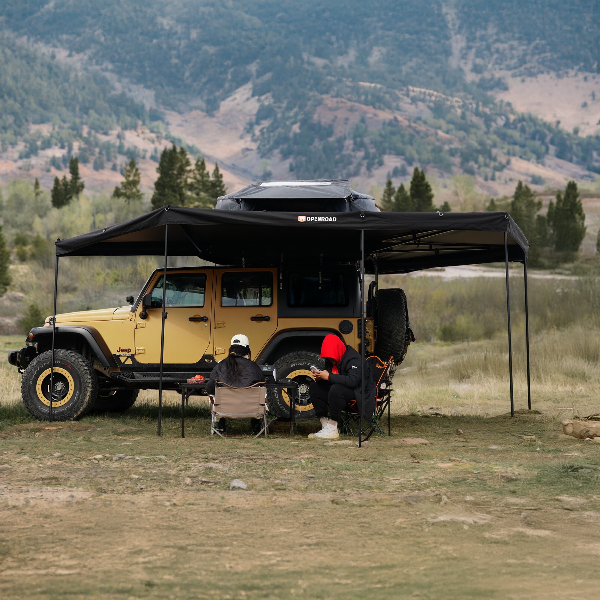 Yellow Jeep under the OpenRoad 270 Awning Plus, with two camping chairs beneath, set against a rugged mountain backdrop