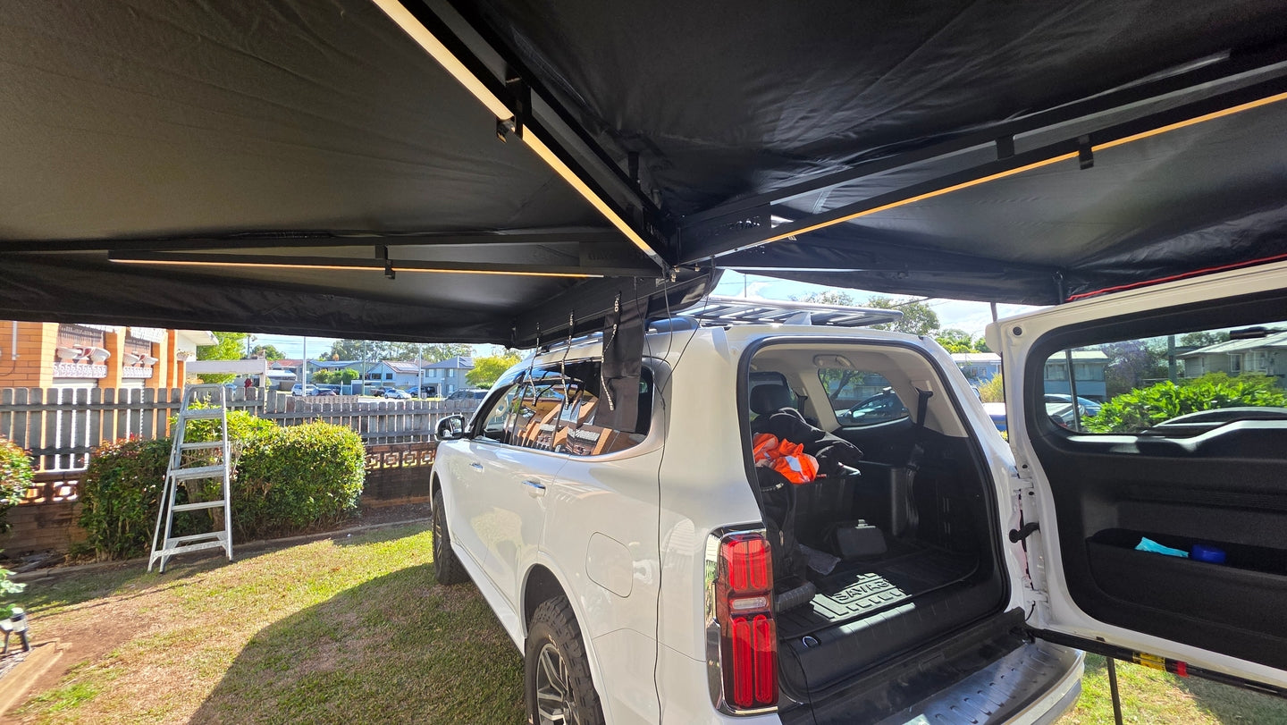 A Kia Sorento fitted with an OPENROAD car awning, providing full shade coverage beside the vehicle during an outdoor setup.