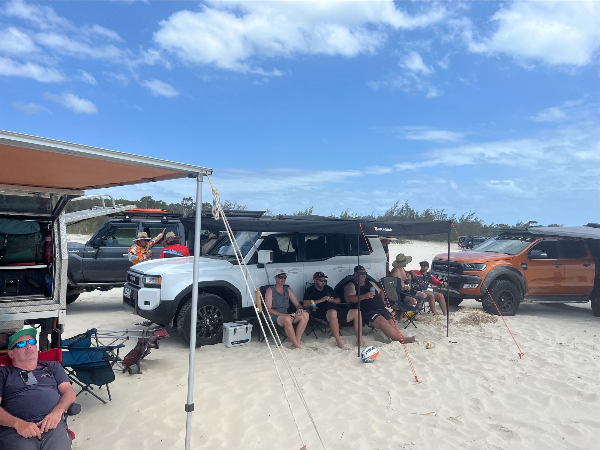 Group camping setup using an OPENROAD 270 awning mounted on a Toyota LandCruiser Prado 250 Series, providing full-side shade on a sunny beach.