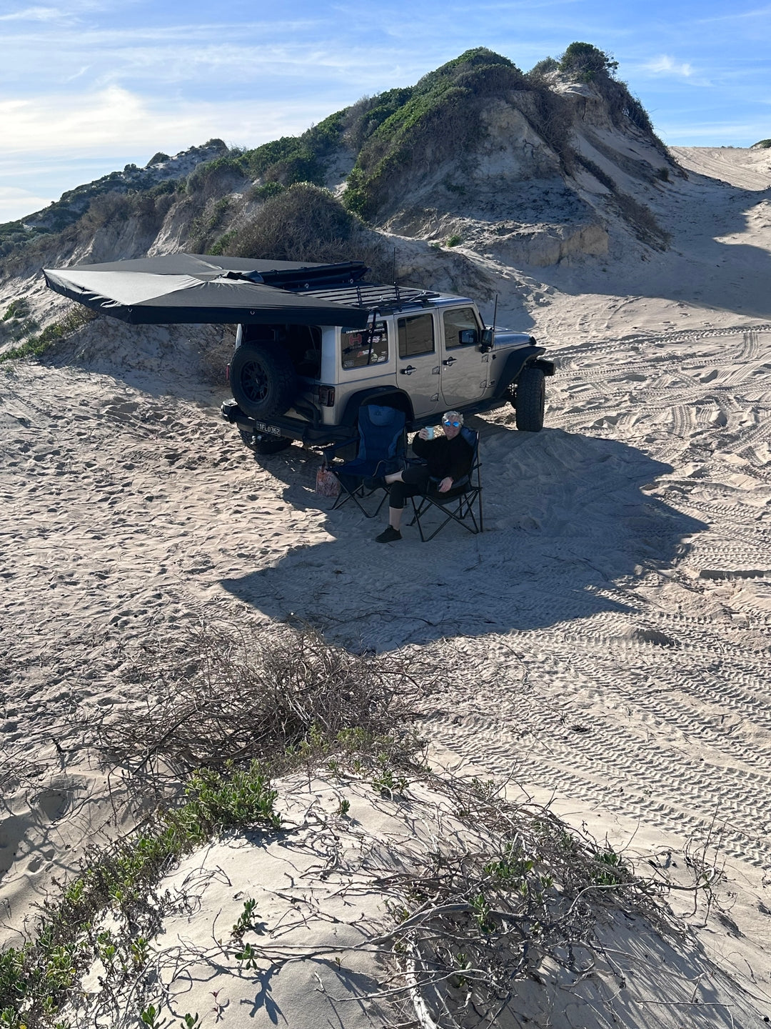 Jeep Wrangler parked on sand dunes with OPENROAD 4wd awning providing shade for beach camping