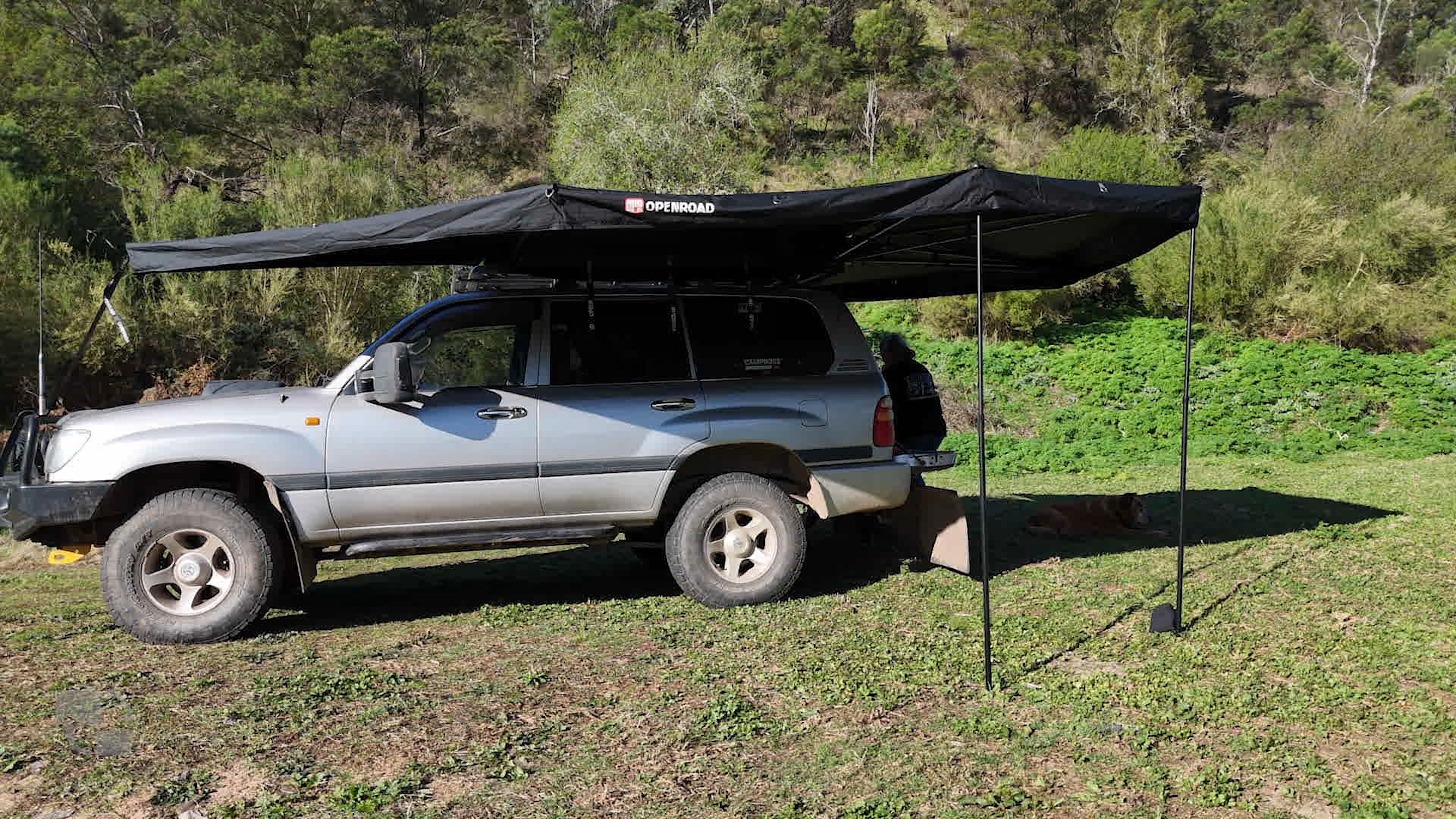 Side view of a Land Cruiser with OPENROAD 270° Awning Plus deployed with two poles, shading a grassy campsite