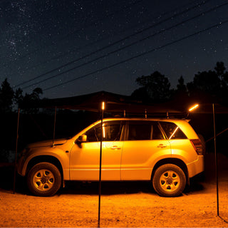 OPENROAD car awning with integrated LED light (amber mode) illuminating a 4x4 SUV campsite under a starry night sky.